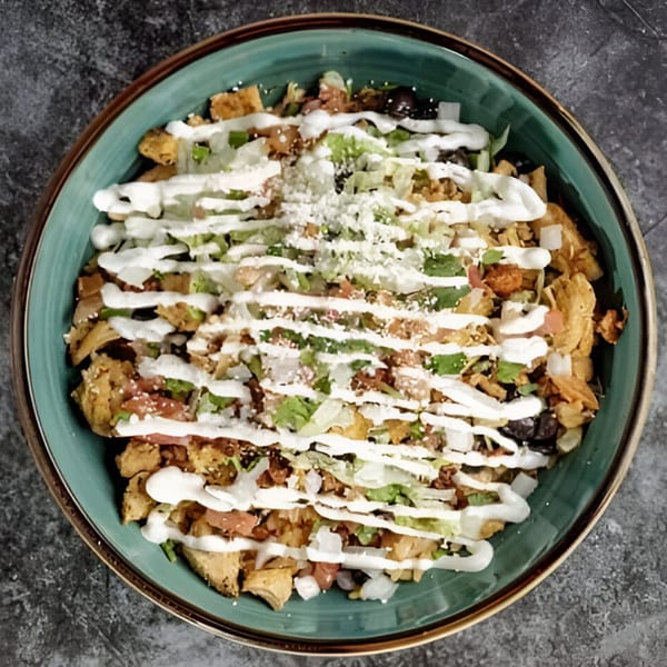 Overhead view of a Mexican dish with chicken, lettuce, tomatoes, and sour cream in a teal bowl.