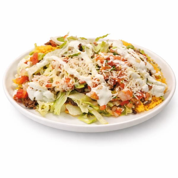 A white plate holds a taco salad with ground beef, lettuce, tomatoes, cheese, and sour cream.