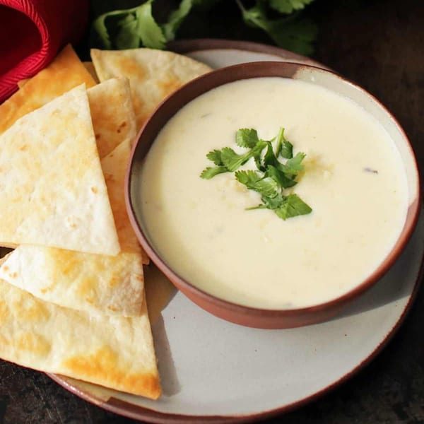 Creamy white queso dip topped with cilantro, served with golden tortilla chips on a rustic plate.
