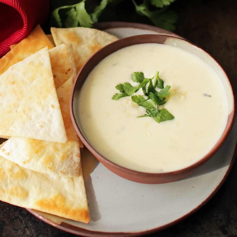 Creamy white queso dip topped with cilantro, served with golden tortilla chips on a rustic plate.