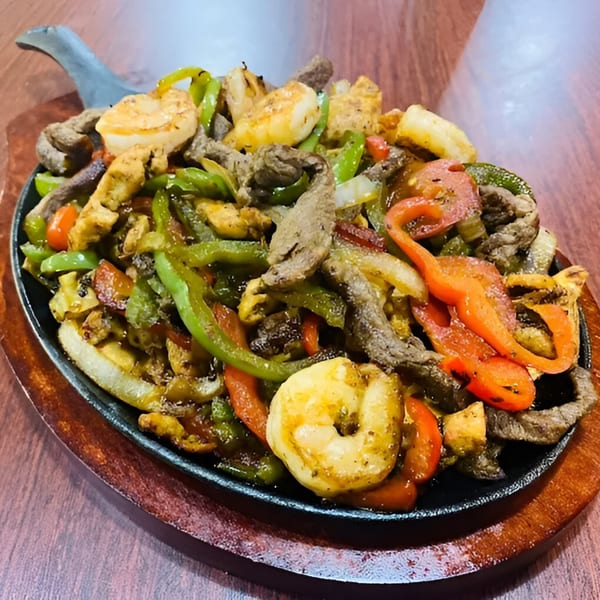Sizzling fajitas with steak, chicken, shrimp, and colorful bell peppers on a cast iron skillet.