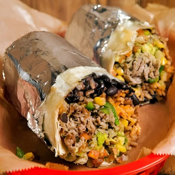 Two large burritos, one unwrapped, filled with meat, rice, beans, and vegetables in a red basket.