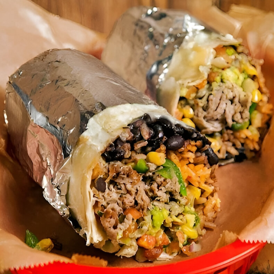 Two large burritos, one unwrapped, filled with meat, rice, beans, and vegetables in a red basket.