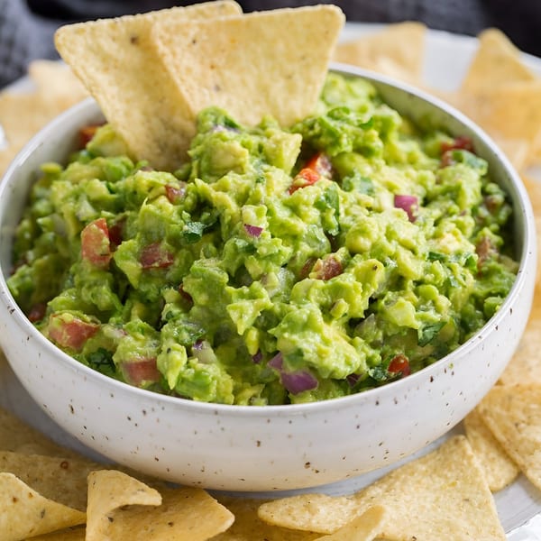 A white bowl filled with chunky green guacamole and surrounded by tortilla chips.