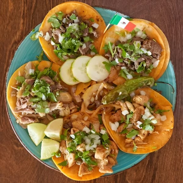 Overhead view of a blue plate with five Fusion Mexican Grill tacos, limes, cucumbers, and a Mexican flag.